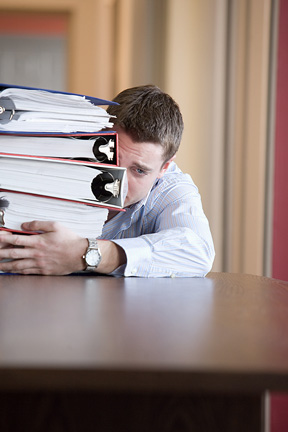 a frightened looking man with a stack of binders