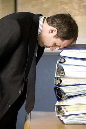 A defeated looking man with his head on a stack of folders