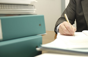 Photo of a man writing with folders and papers around him